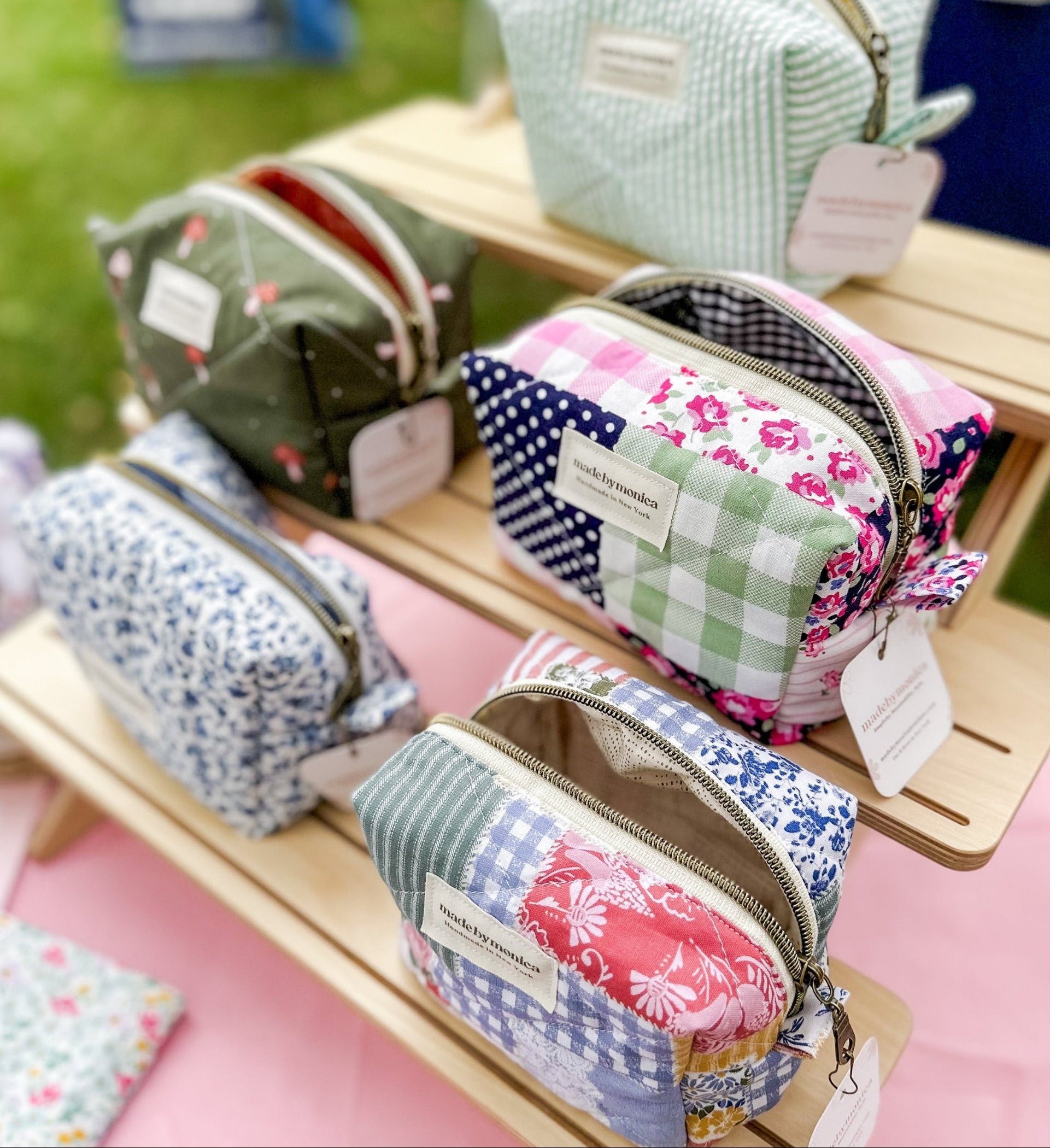 Colorful fabric pouches on a wooden stand with tags, set against a blurred outdoor background.