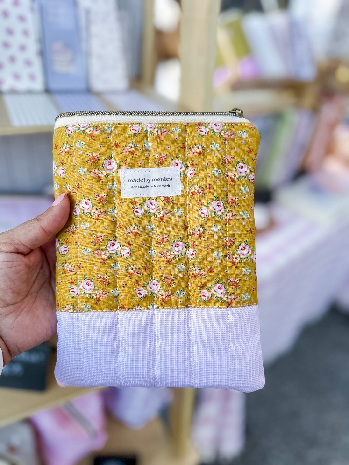 Hand holding a yellow floral-patterned pouch with a white label.