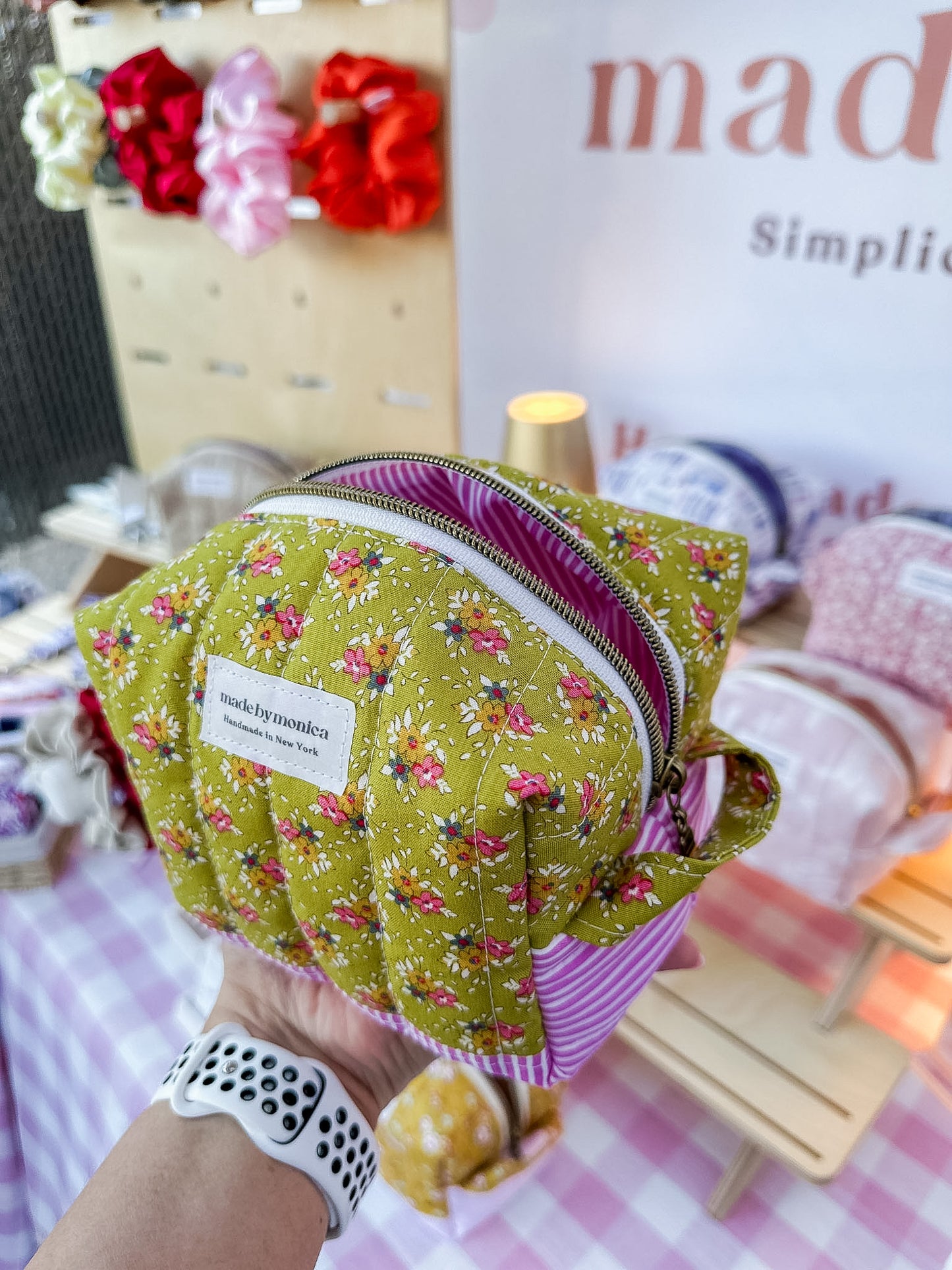 Handmade green fabric pouch with floral pattern held by a person, with a blurred background.