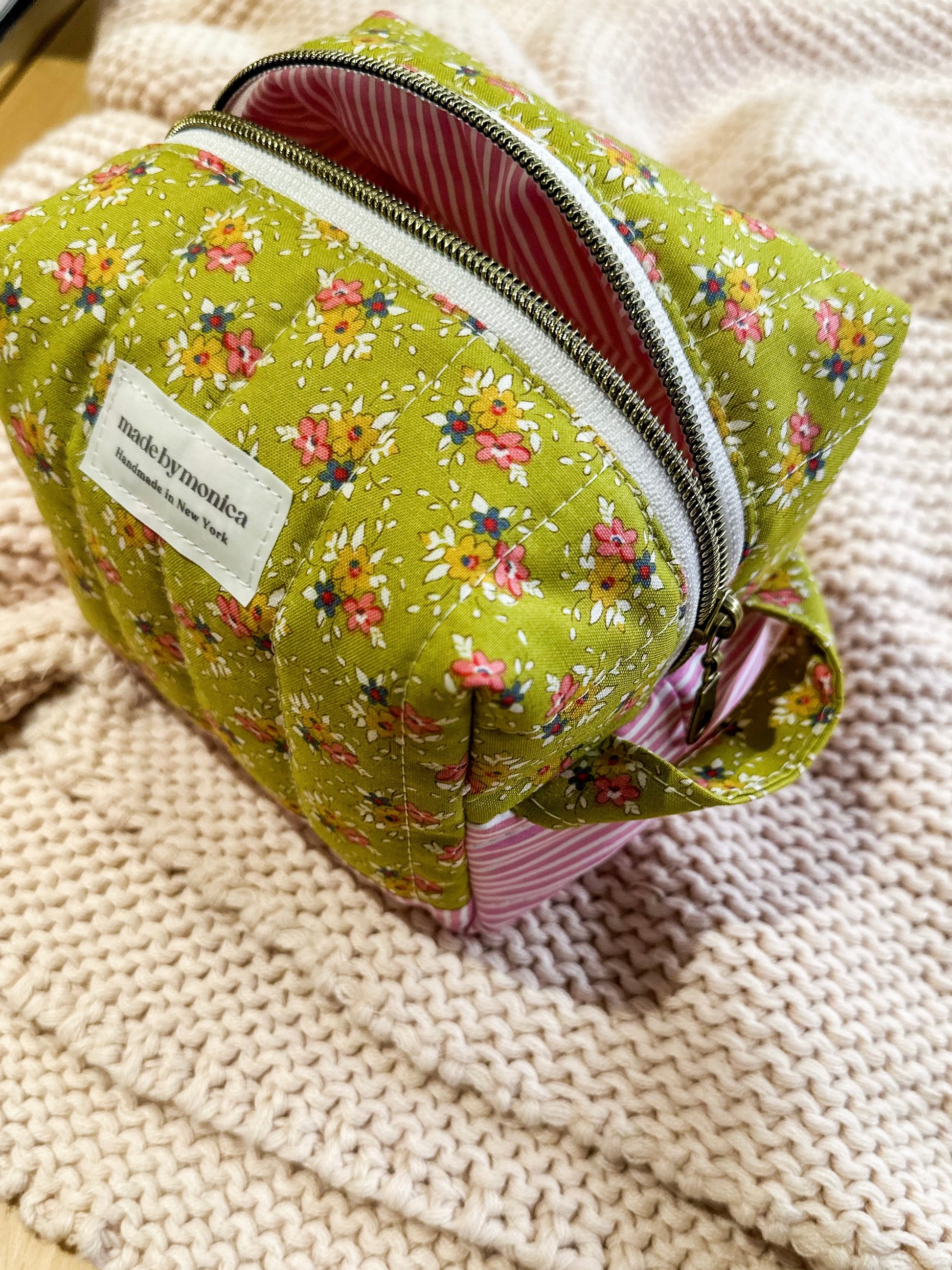 Green floral-patterned pouch with a visible brand label on a textured beige surface