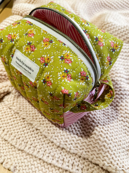 Green floral-patterned pouch with a visible brand label on a textured beige surface