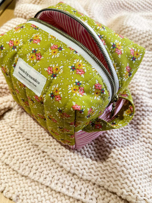 Green floral-patterned pouch with a visible brand label on a textured beige surface