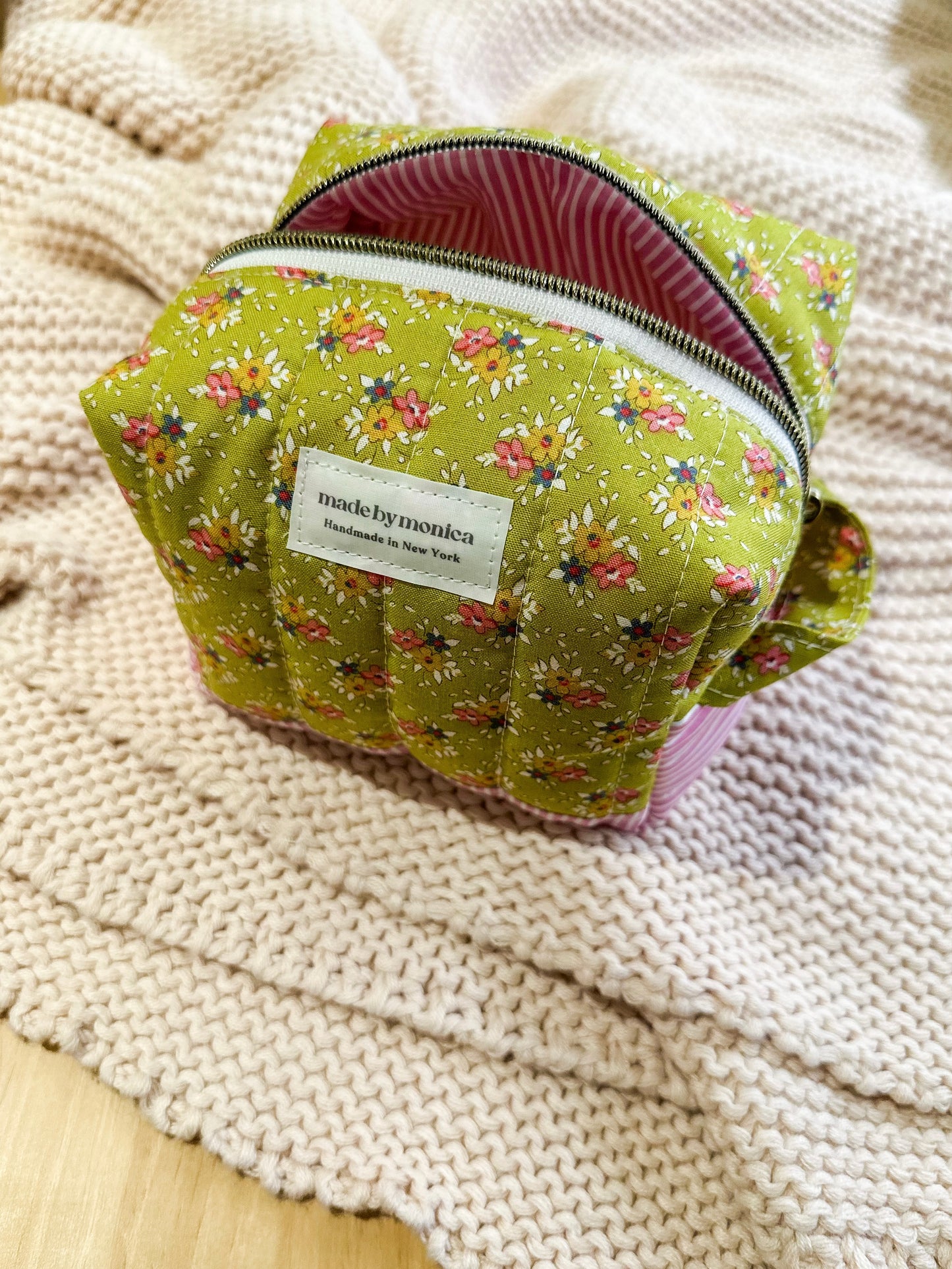 Green floral-patterned makeup bag with a visible brand label on a textured beige surface.