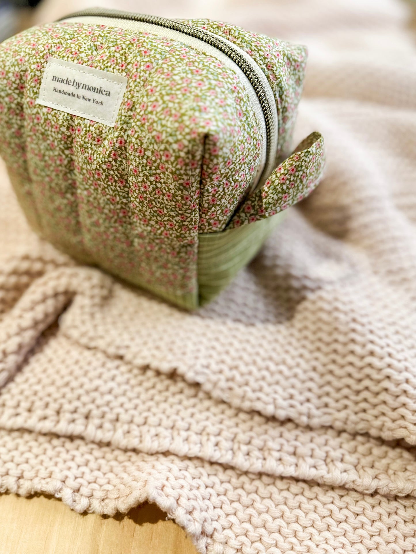 Small green fabric pouch with floral pattern on a beige textured surface