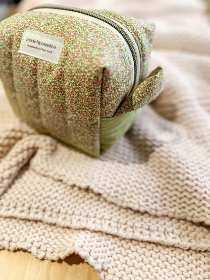 Small green fabric pouch with floral pattern on a beige textured surface
